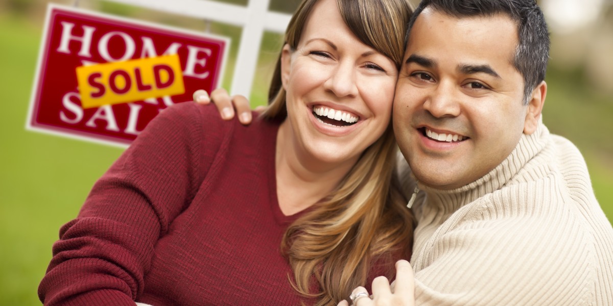 Couple in front of sold house sign smiling