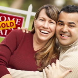 Couple in front of sold house sign smiling