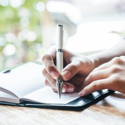 Person writing with white pen in notebook