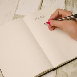 Woman's hand writing "My Plan" in notebook