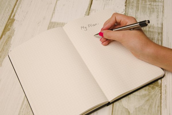 Woman's hand writing "My Plan" in notebook