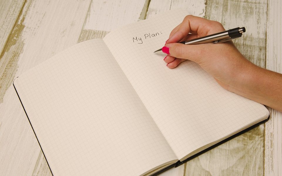 Woman's hand writing "My Plan" in notebook