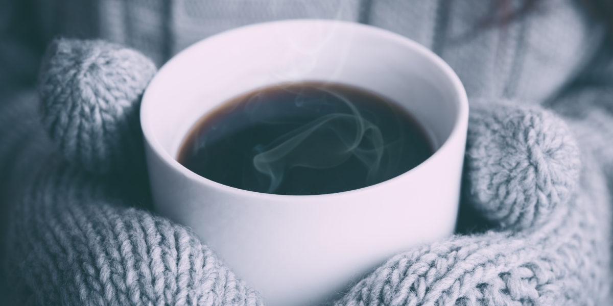 Hands in mittens holding a warm cup of coffee.