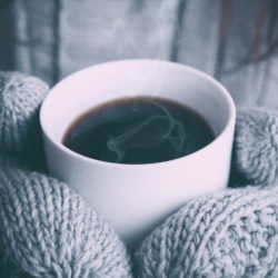 Hands in mittens holding a warm cup of coffee.