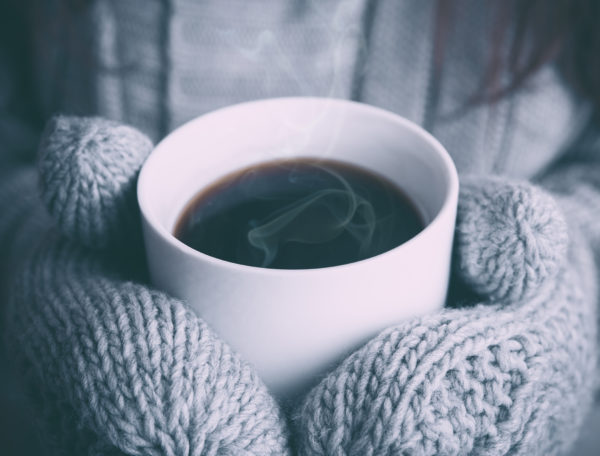 Hands in mittens holding a warm cup of coffee.