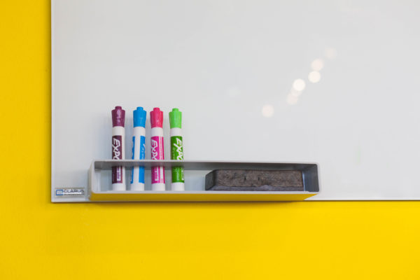 A white board on a yellow wall with markers and an erraser