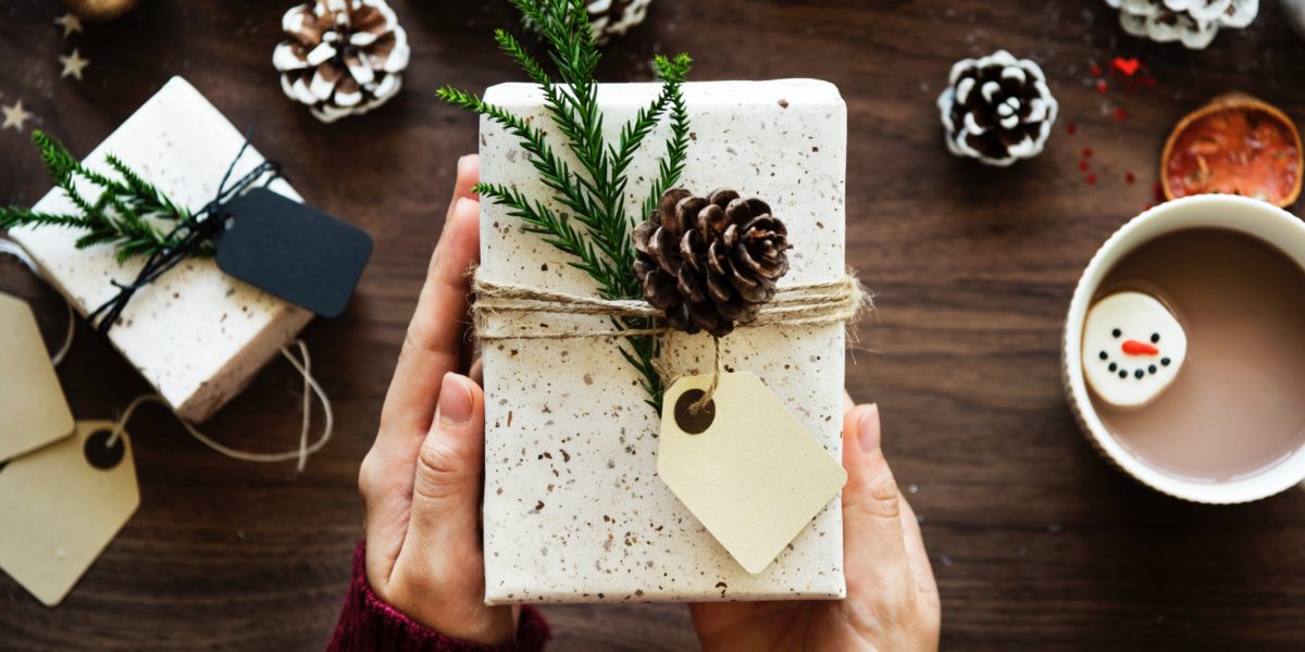 hands holding a gift decorated with fir cones and needles