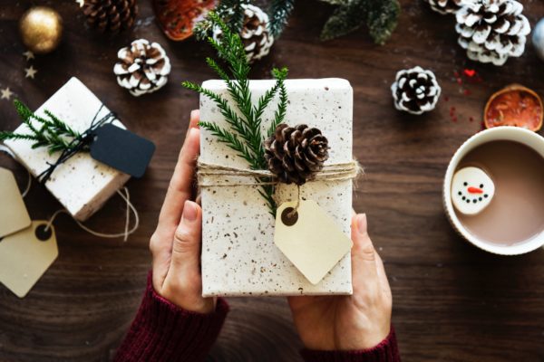 hands holding a gift decorated with fir cones and needles
