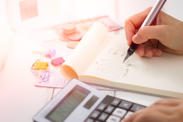 calculator, hand with pen writing in notebook