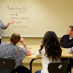 Young Woman at white board presenting budgeting information to college students