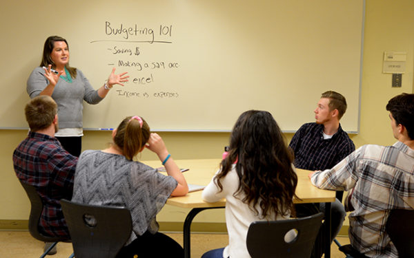 Young Woman at white board presenting budgeting information to college students