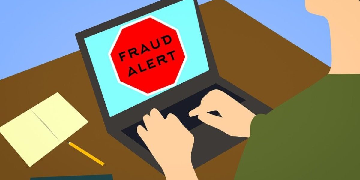 illustration of a red (stop) fraud alert sign on computer with person's hands on keyboard