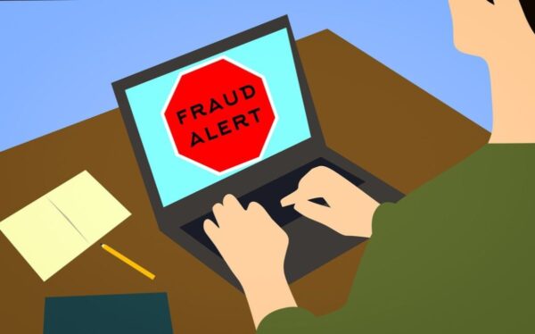 illustration of a red (stop) fraud alert sign on computer with person's hands on keyboard