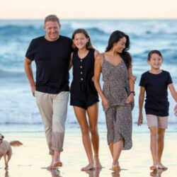 family of four walking on beach with small dog and waves in the background
