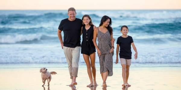 family of four walking on beach with small dog and waves in the background