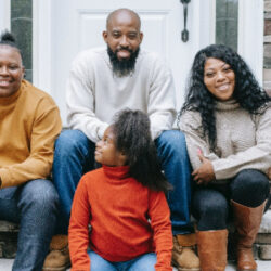 African-American family of four sitting on stone steps of house, smiling