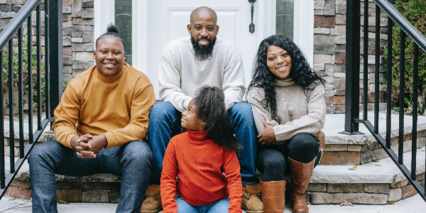 African-American family of four sitting on stone steps of house, smiling