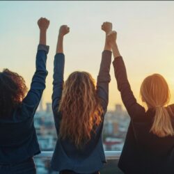 photo of three women with backs to camera facing the sun with arms raised