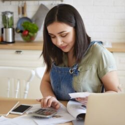 woman sitting at the kitchen table looking at receipts and using a calculator