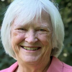 Barbara is wearing a pink collared shirt and is smiling at the camera