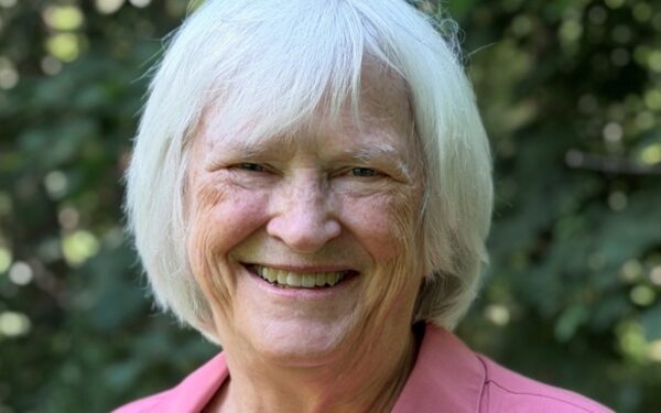 Barbara is wearing a pink collared shirt and is smiling at the camera