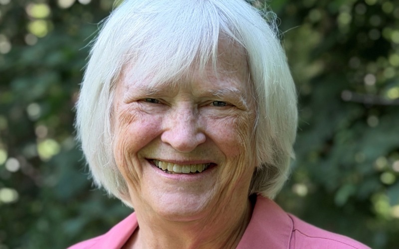 Barbara is wearing a pink collared shirt and is smiling at the camera